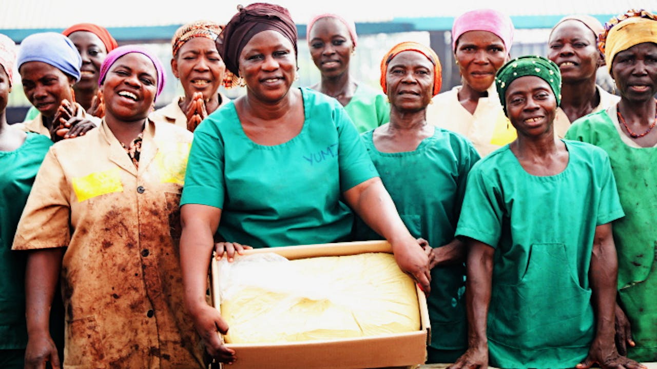 Zakaria Adama Lacera holds a box of creamy white shea butter surrounded by women workers who have helped to make it. They all wear differently coloured headscarves.